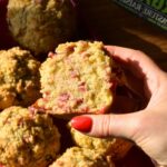 A hand holding an orange cranberry yogurt muffin.