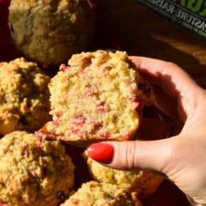 A hand holding an orange cranberry yogurt muffin.