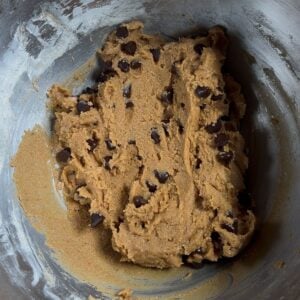 A stainless steel mixing bowl filled with easy protein cookie dough, with visible chocolate chips scattered throughout the thick, light brown mixture.