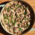 A large pan filled with creamy chicken and rice, red kidney beans, and garnished with fresh parsley, sits on a wooden surface.