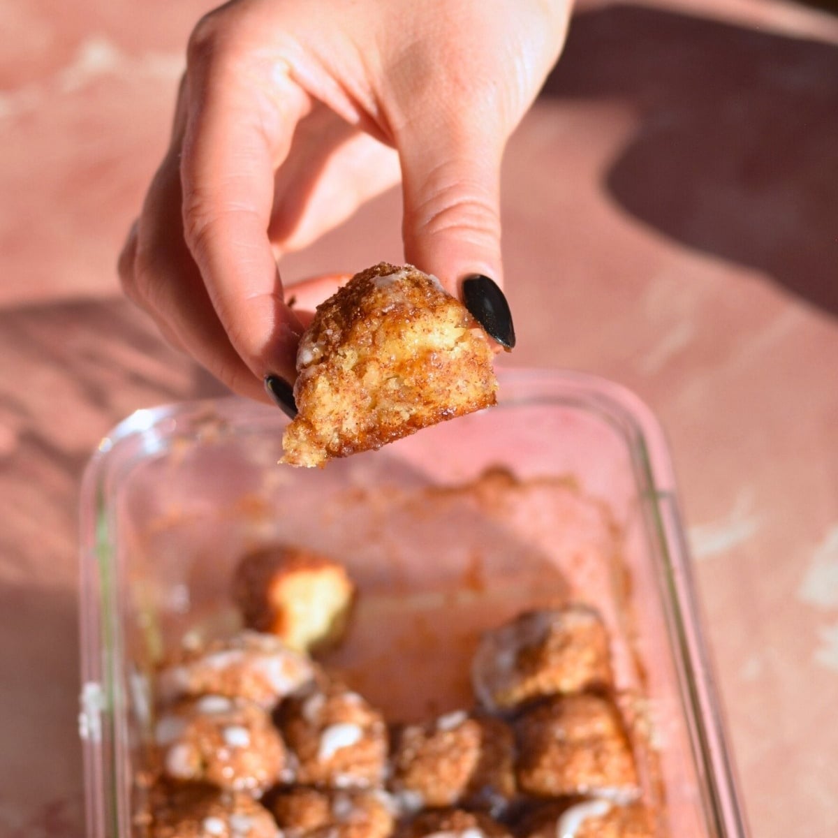 A hand with black nail polish holding a cinnamon roll bite.