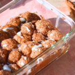Cinnamon roll bites with white frosting on top in a rectangular glass container.