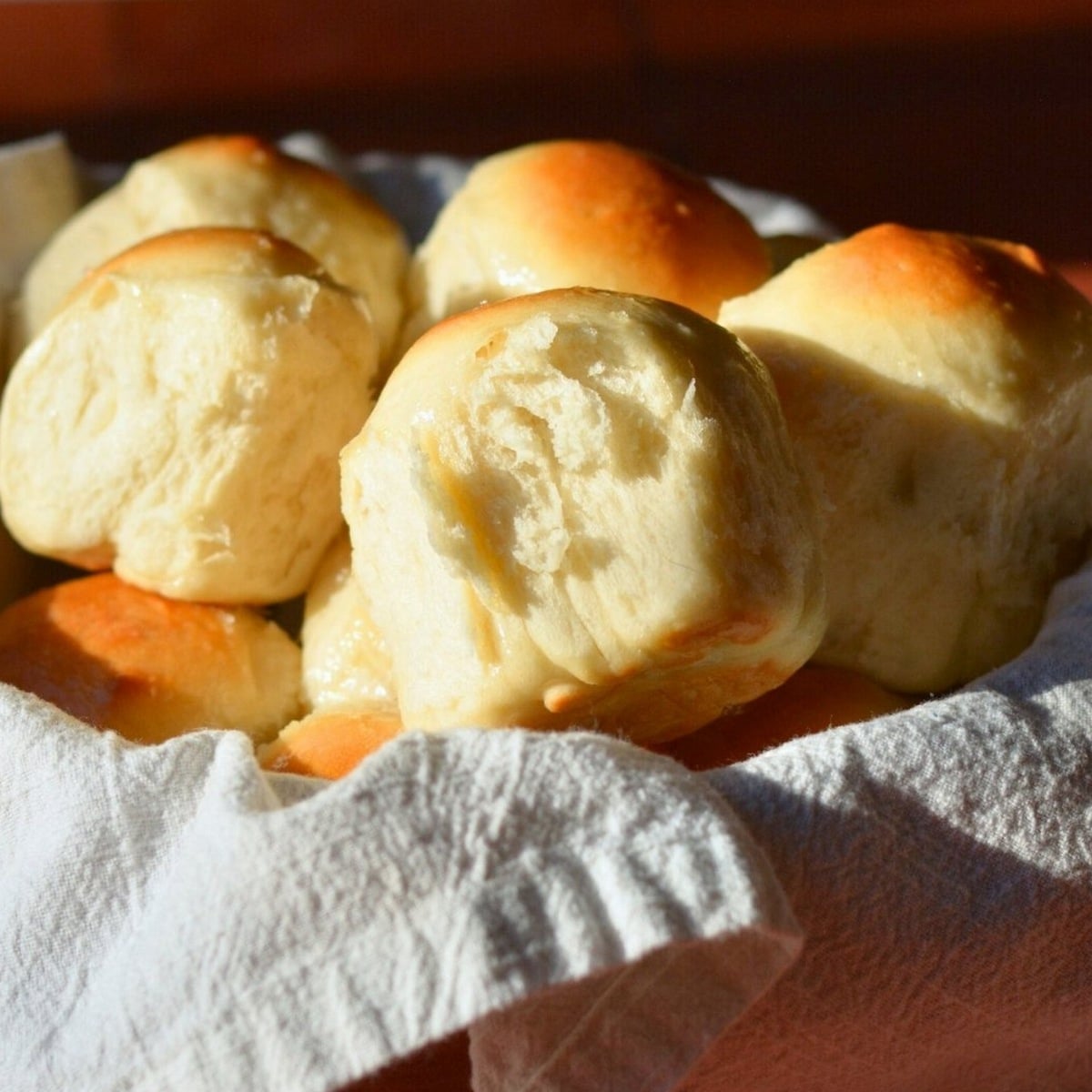 A bowl lined with a white napkin that's filled with fluffy protein dinner rolls.