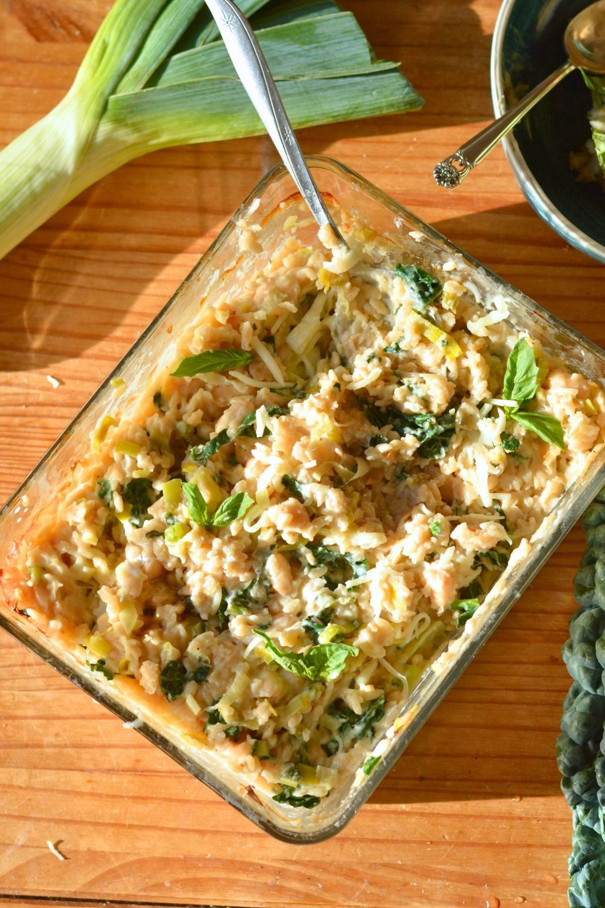 A rectangular glass dish filled with white bean casserole with shredded basil on top.