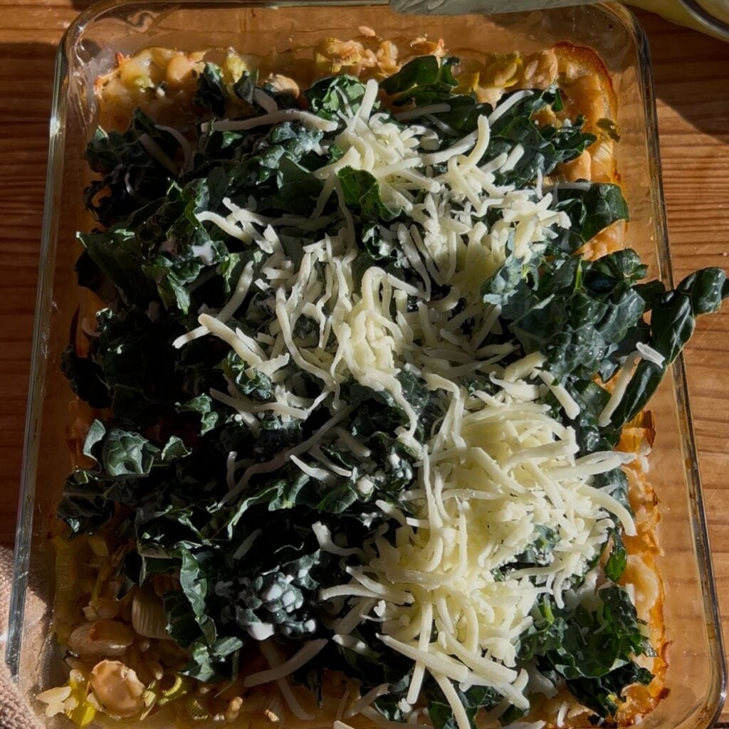 A casserole dish with kale and cheese on top of a white bean casserole.