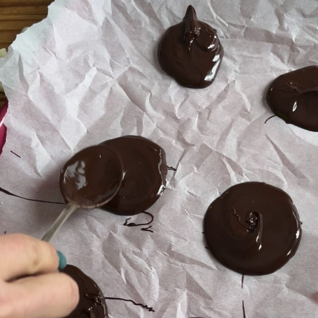 Hand spreading out chocolate circles on a tray with a spoon.