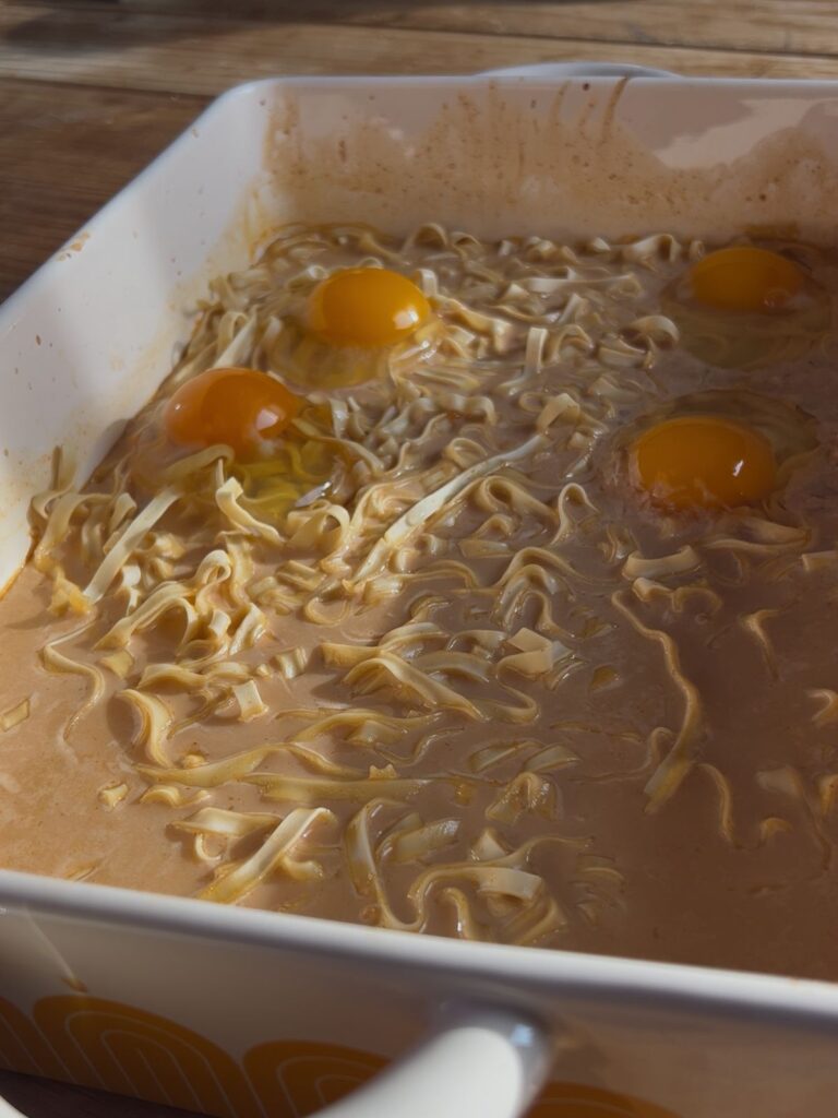A pan with noodles and 4 eggs in it before baking.