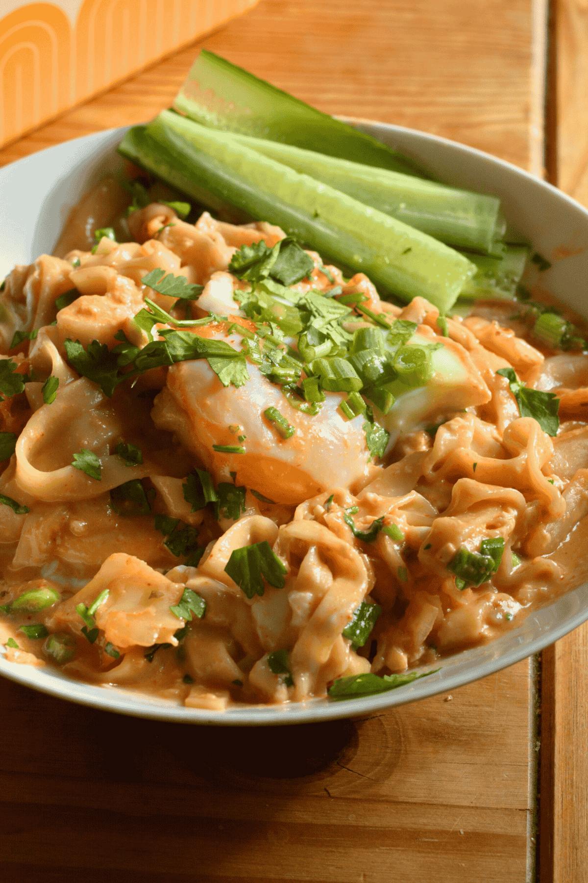A bowl of protein peanut ramen noodles with an egg, diced green onion, and sliced cucumbers.