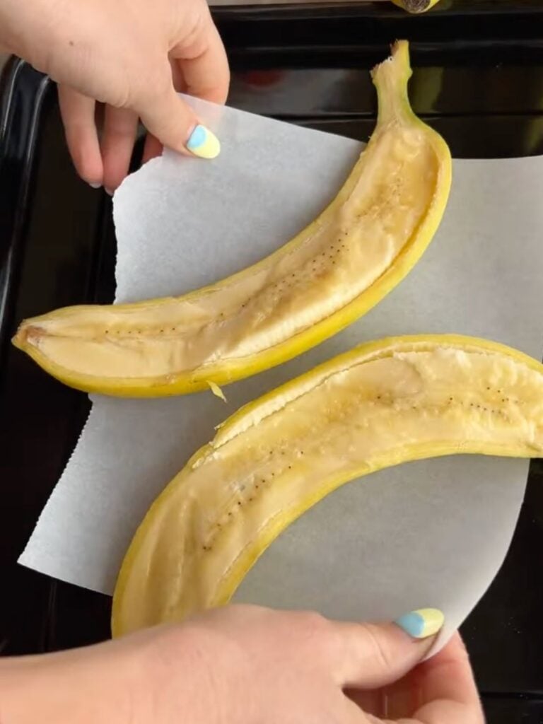 Hands placing a banana cut lengthwise onto an air fryer tray.
