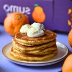 A stack of orange protein pancakes on a purple background.