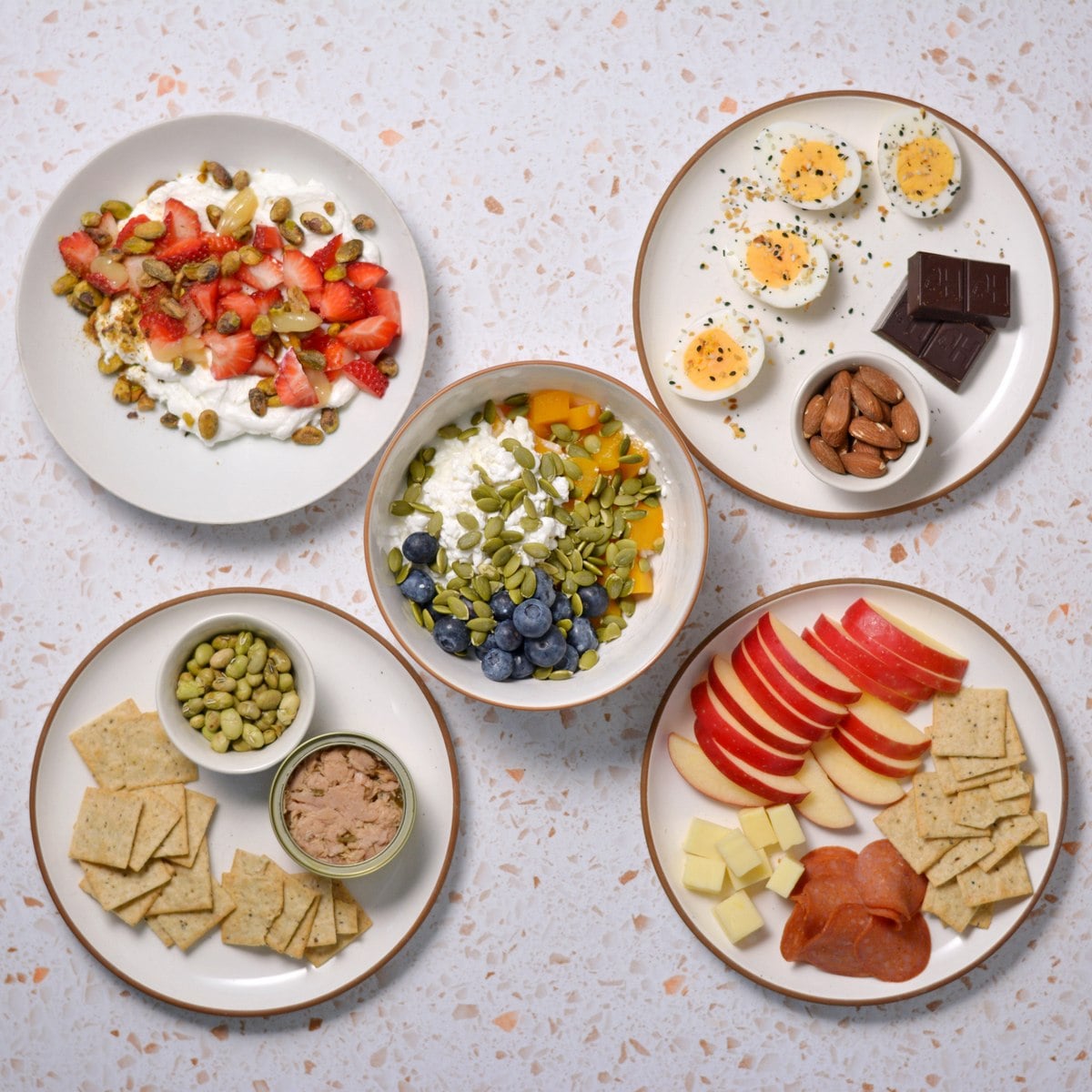 5 plates and bowls with a variety of high protein and high fiber snacks.