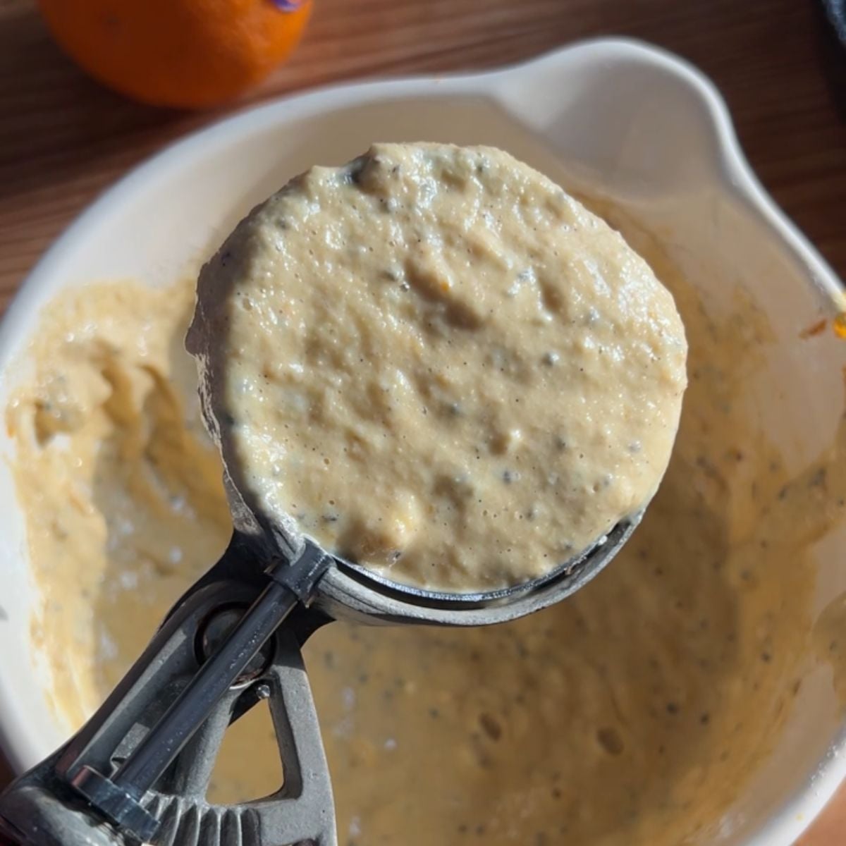 An ice cream scooping scooping the orange pancake batter to show how thick it is.