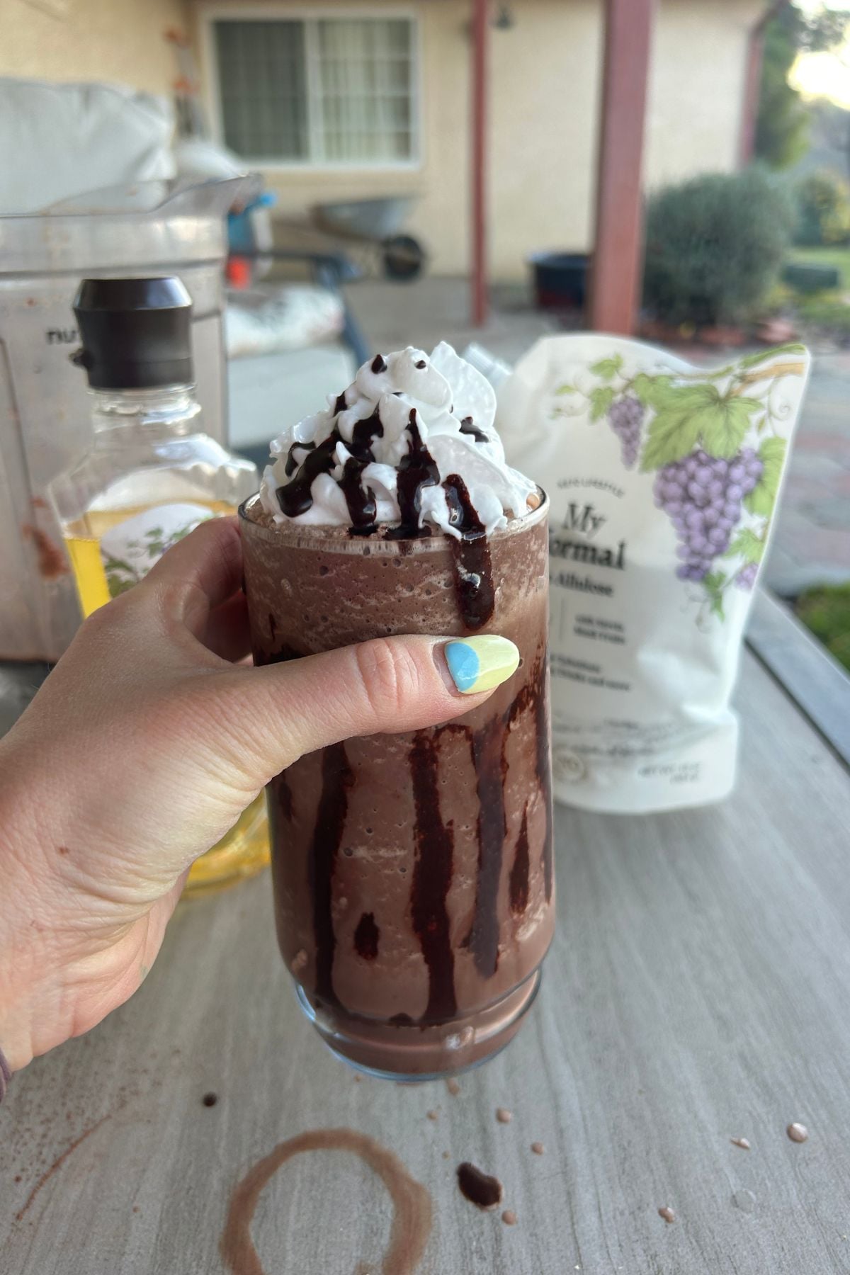 Hand holding a dairy-free protein frappuccino with chocolate drizzle in glass