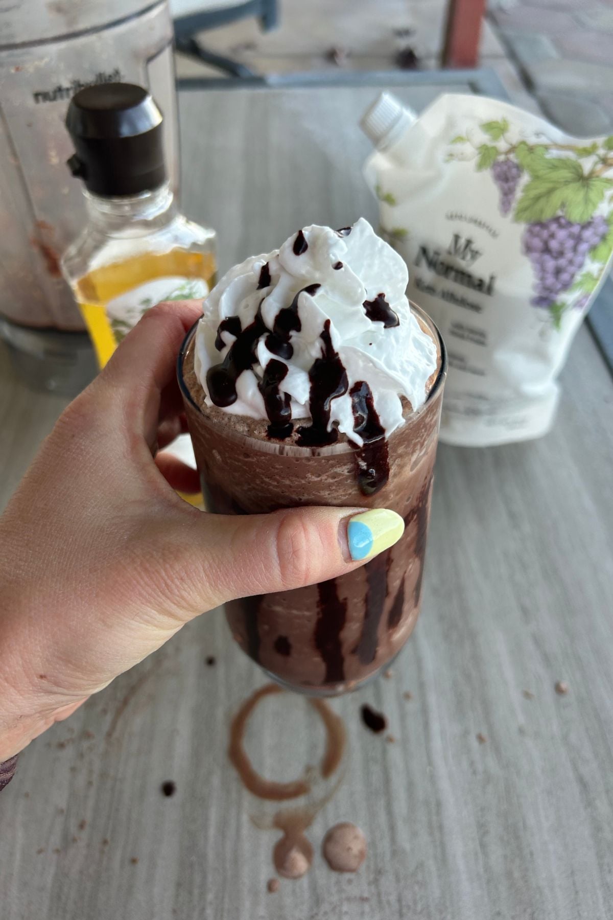 Hand holding a dairy-free protein frappuccino with chocolate drizzle in glass