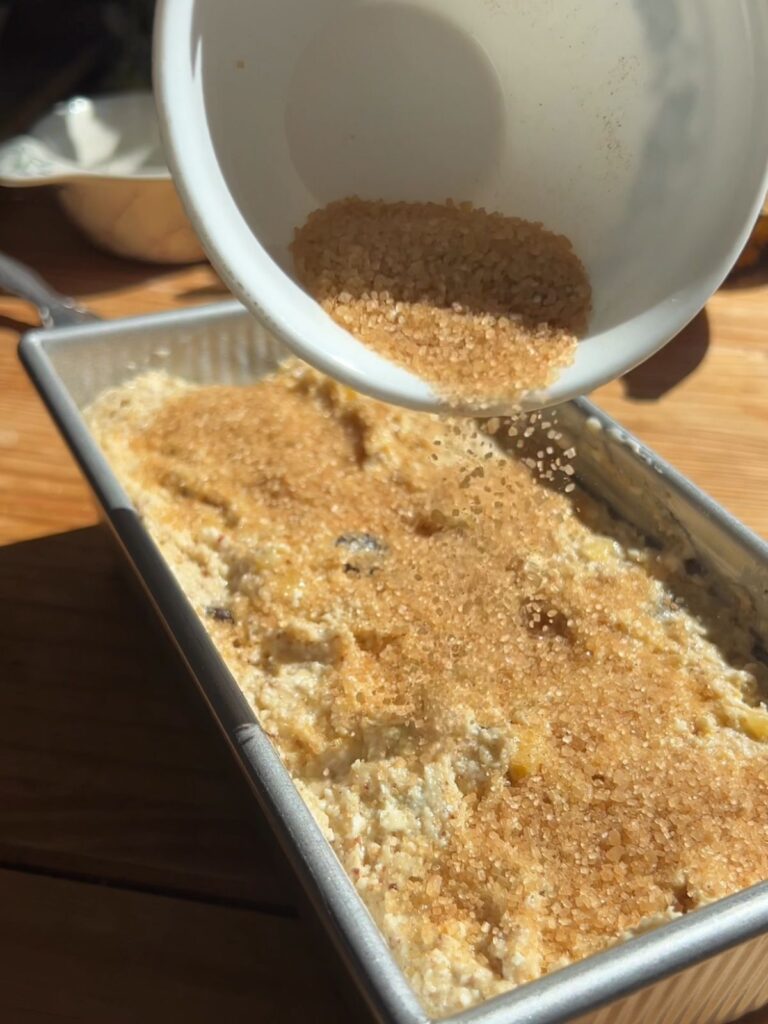 Sprinkling sugar on top of cottage cheese banana bread batter in pan.