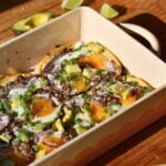 A casserole dish with huevos rancheros consisting of egg, refried beans, avocado, onion, and cilantro.