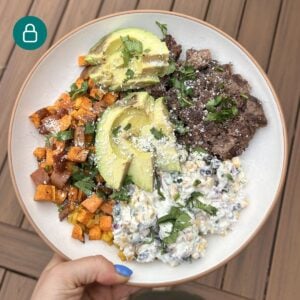 A bowl with street corn dip, sweet potatoes, burger, and avocado.