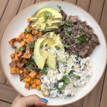 A bowl with street corn dip, sweet potatoes, burger, and avocado.