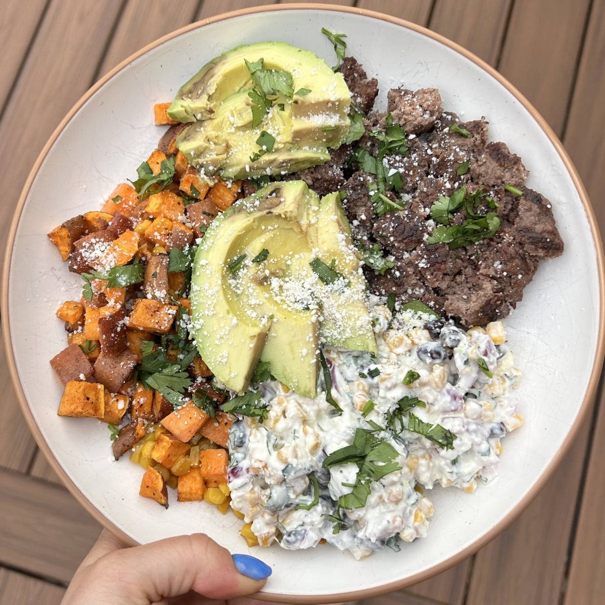 A bowl with street corn dip, sweet potatoes, burger, and avocado.