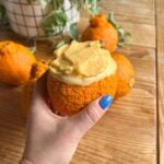 A hand holding the cottage cheese ice cream in the orange peel cup.