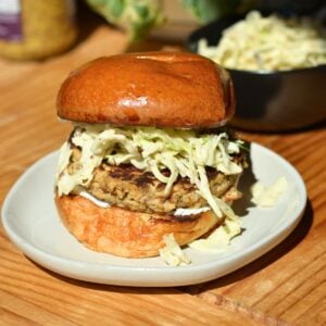 A canned salmon burger with slaw on a white plate.