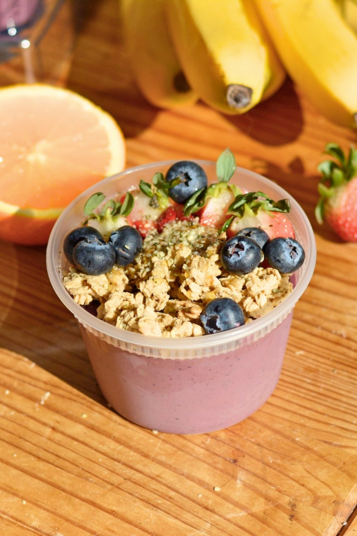 A protein acai bowl in a plastic tub with granola and berries on top.