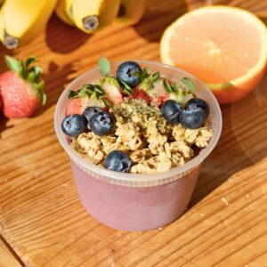 A protein acai bowl in a plastic tub with granola and berries on top.