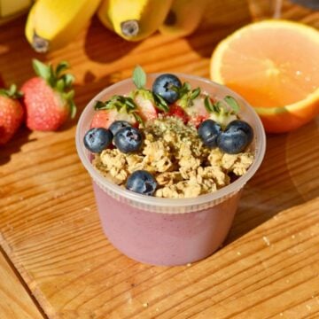 A protein acai bowl in a plastic tub with granola and berries on top.
