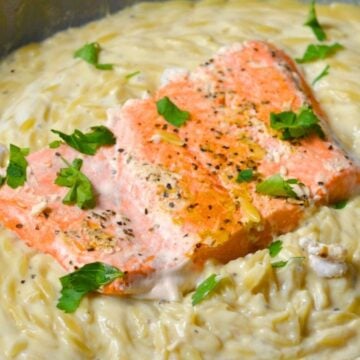A salmon fillet in a pan with creamy Greek yogurt alfredo orzo.
