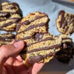 A healthy samoa cookie with a bite taken out being held by a hand.