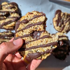 A healthy samoa cookie with a bite taken out being held by a hand.
