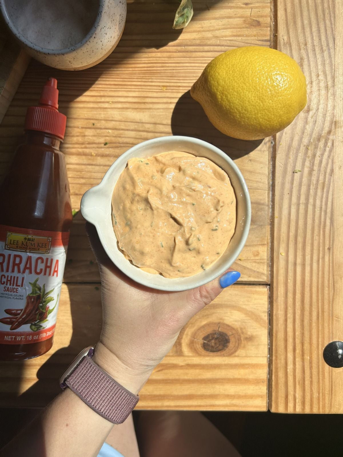 a hand holding a bowl of greek yogurt sriracha sauce.