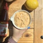 a hand holding a bowl of greek yogurt sriracha sauce.