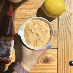 a hand holding a bowl of greek yogurt sriracha sauce.