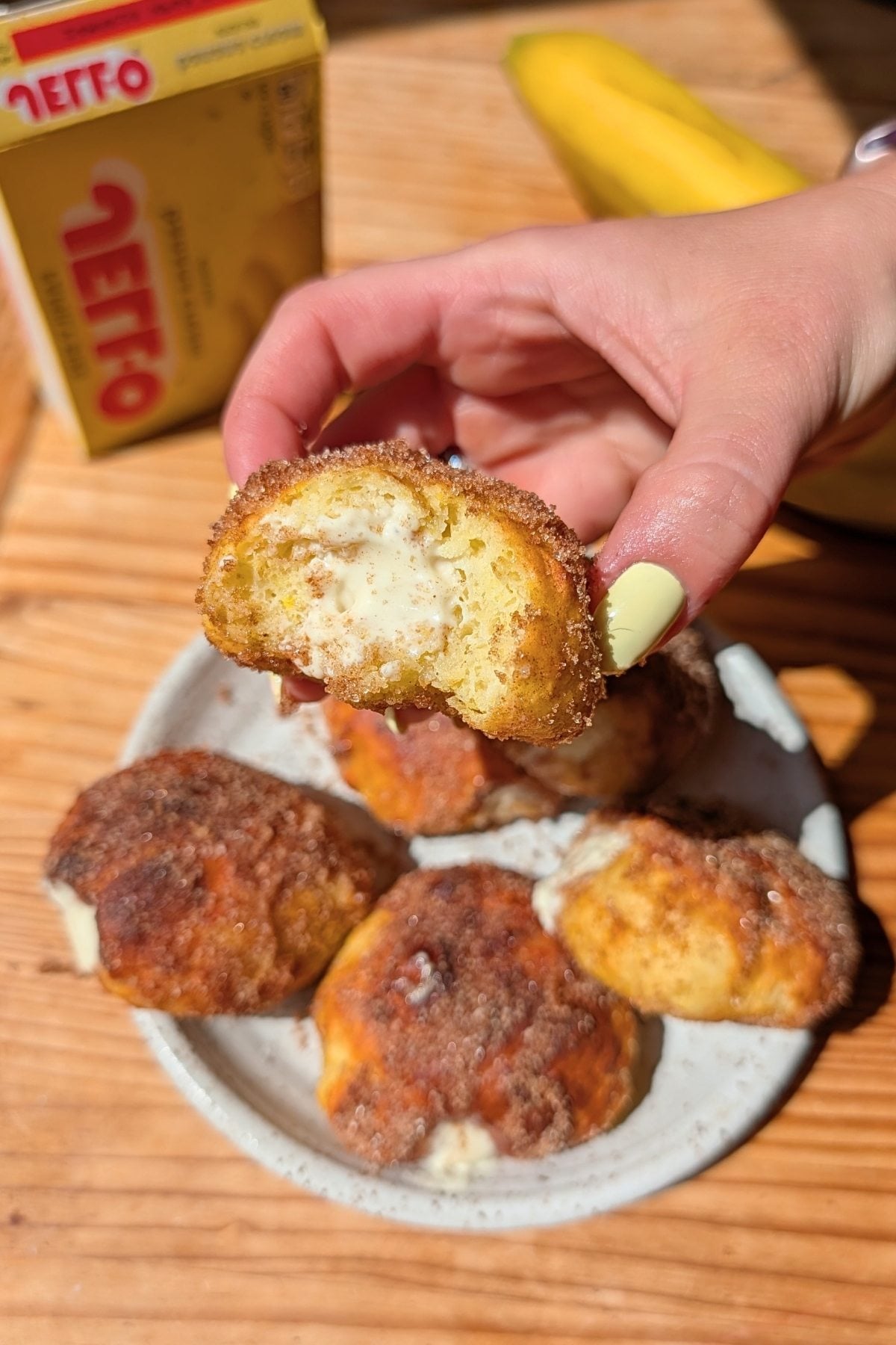 Hand holding banana pudding donut with the filling coming out.