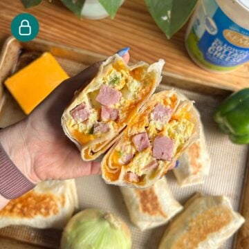 Hand holding denver omelet breakfast burrito cut open.