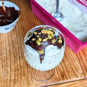 A cup with Greek yogurt ice cream with chocolate and pistachios on top.