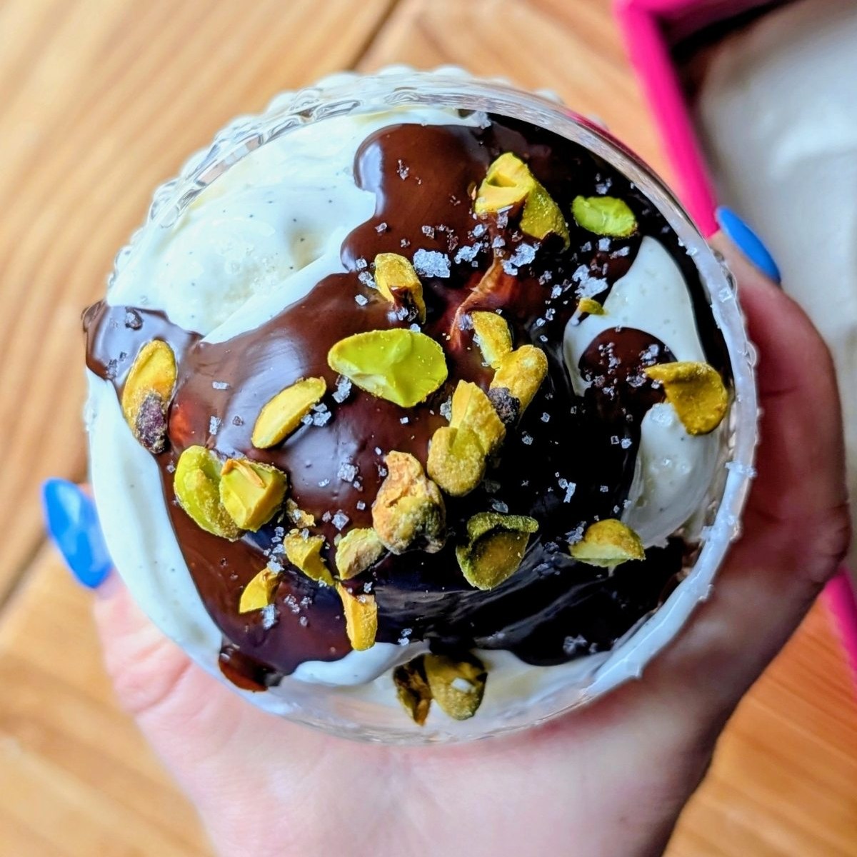 A hand holding a cup of Greek yogurt ice cream with chocolate and pistachios on top.