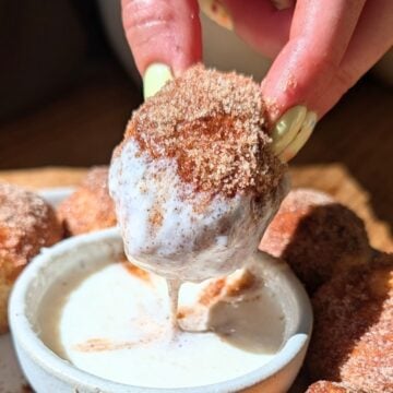 A hand dipping a protein pretzel bite into protein frosting.