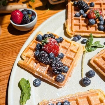 four protein waffles with berries and powdered sugar on top.