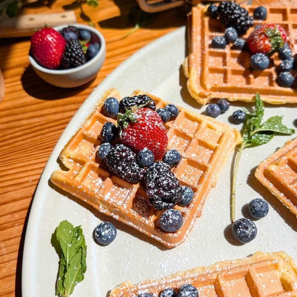 four protein waffles with berries and powdered sugar on top.