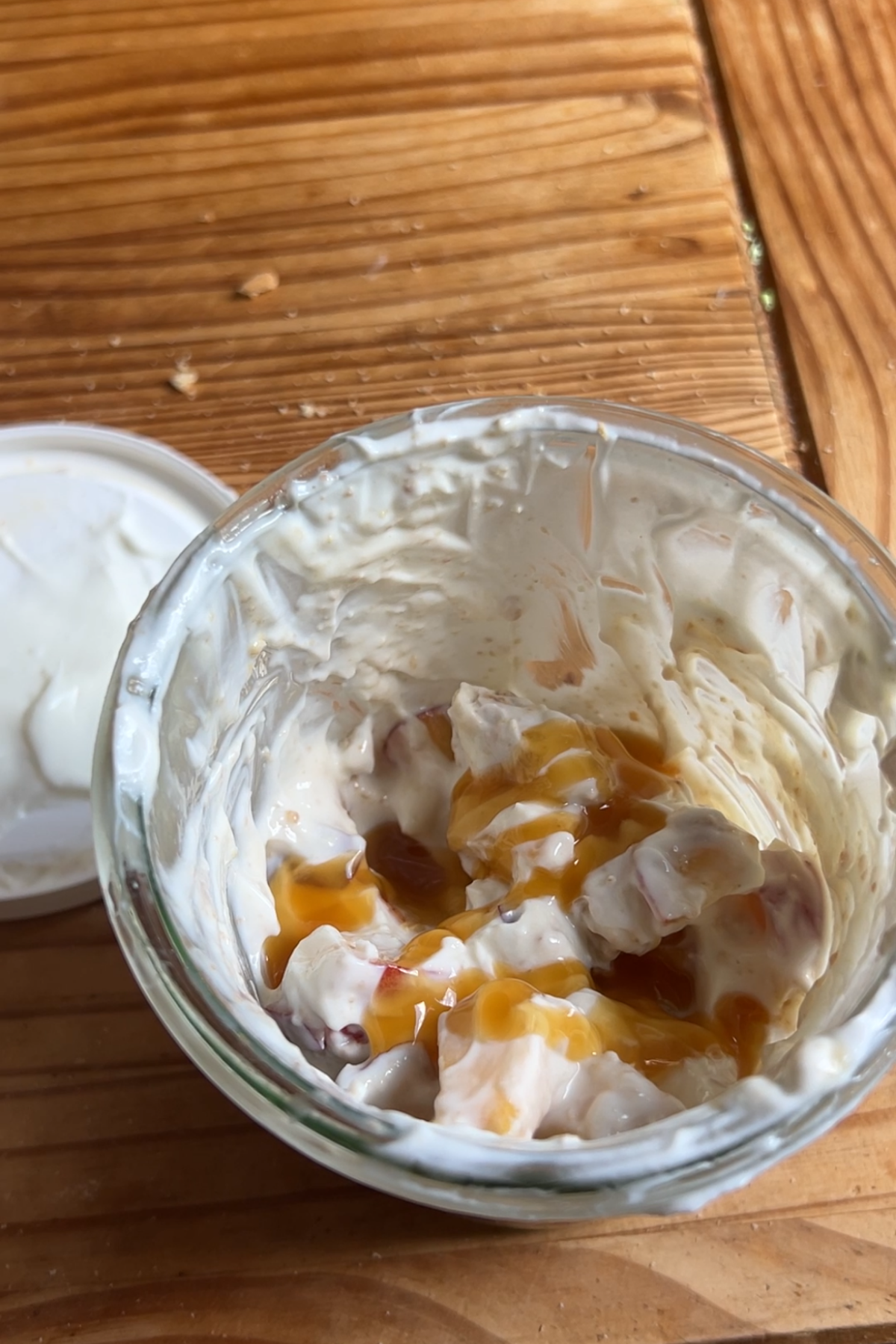 A jar with peach salad topped with extra caramel sauce.