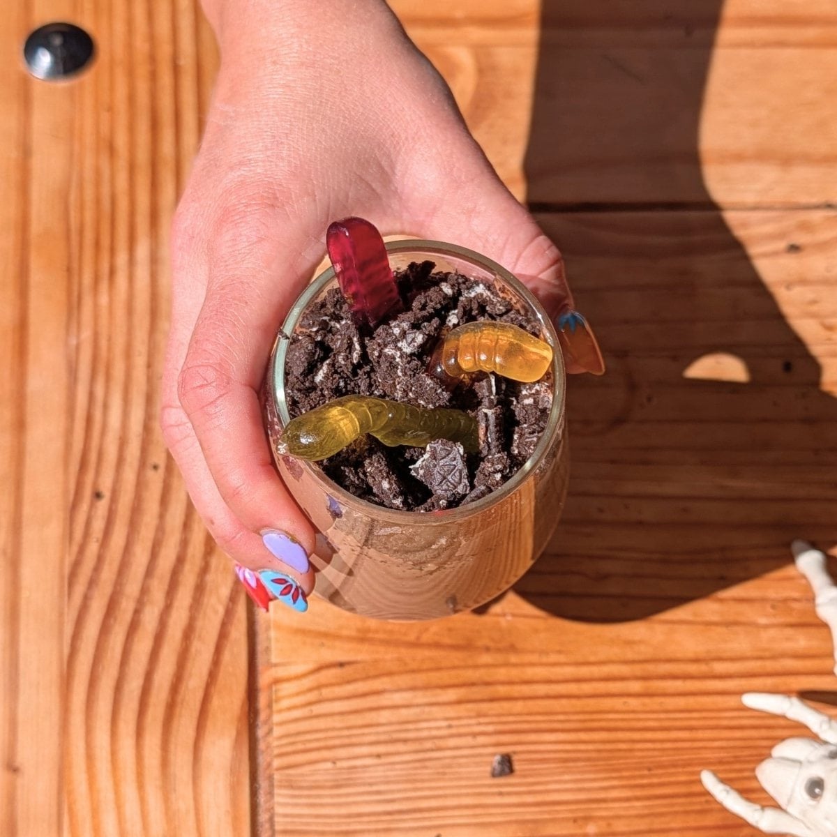 A hand holding a protein dirt cup with gummy worms.